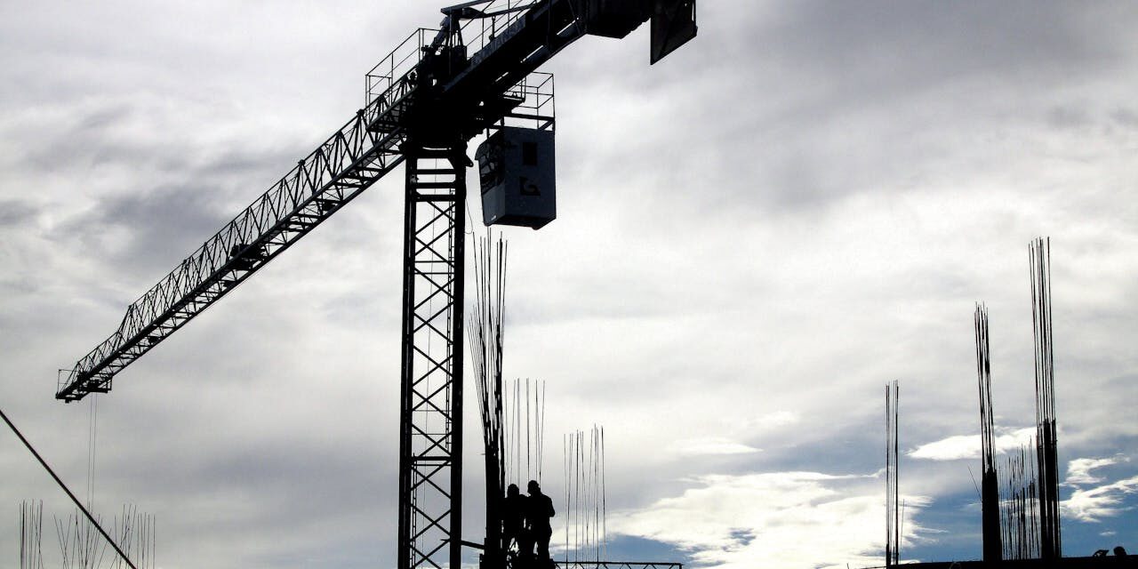 Bouwplaats met silhouet van een torenkraan en bouwvakkers bij schemerlicht, focus op bouwkraan kopen.
