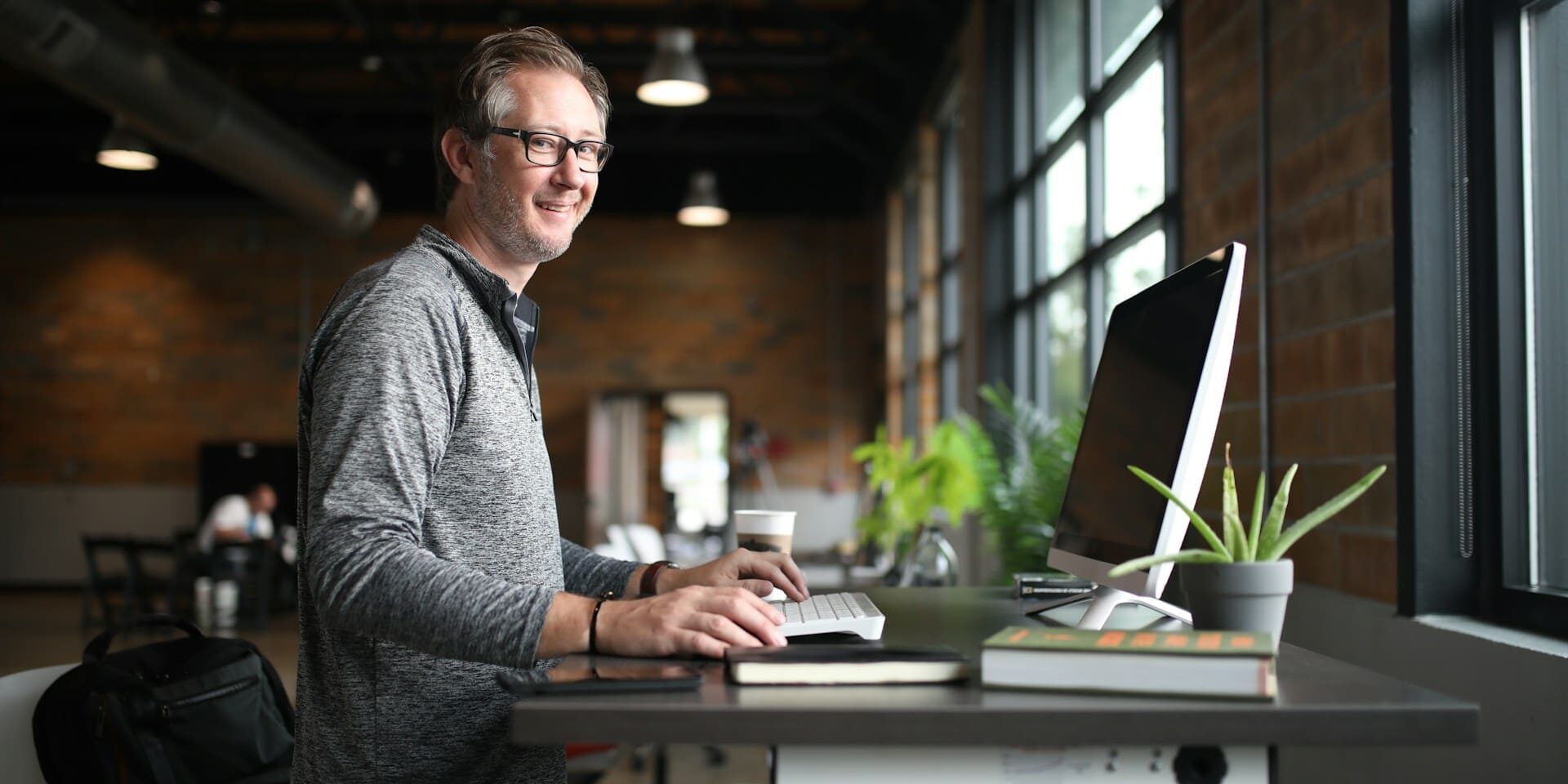 Man werkt staand achter ergonomisch bureau met computer, als voorbeeld van bewust bewegen op het werk.