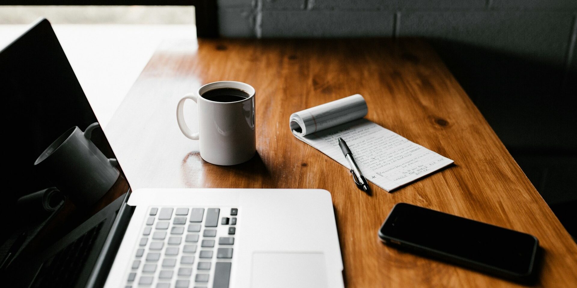 Werkplek met laptop, koffie, notitieblok en telefoon – passend bij het opstellen van herkenbare vacatures.