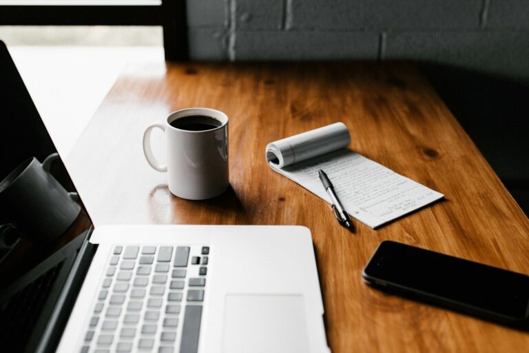 Werkplek met laptop, koffie, notitieblok en telefoon – passend bij het opstellen van herkenbare vacatures.