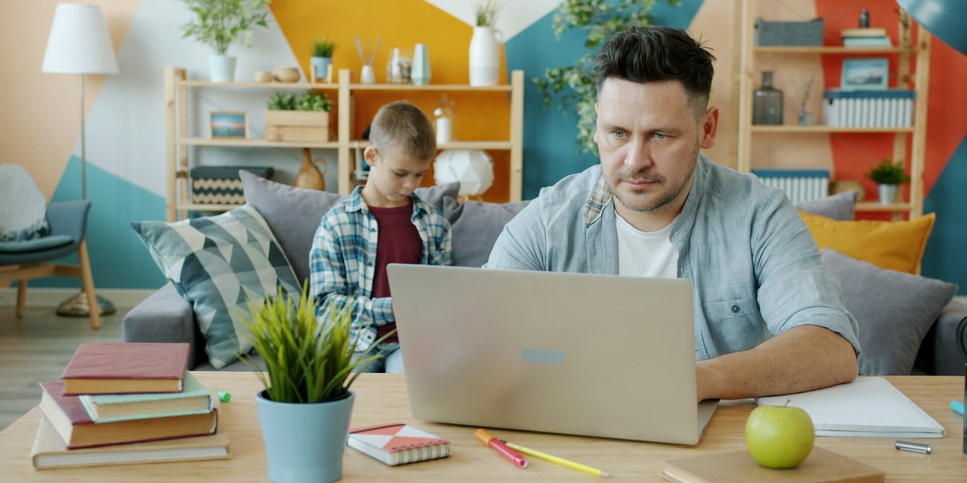 Vader werkt thuis met laptop terwijl zijn kind op de achtergrond speelt, illustratie van thuiswerken en gezin combineren